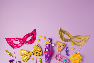 Purim holiday concept with carnival mask and party supplies on purple background. Top view from above with copy space