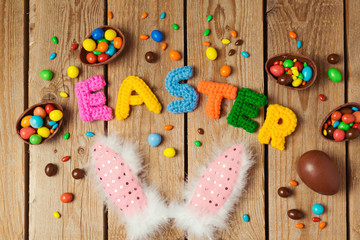 Fototapeta na wymiar Easter holiday concept with chocolate eggs and bunny ears on wooden background. Top view from above