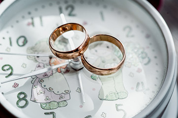 macro of wedding rings next to the flowers and romantic clock
