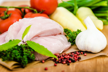 Raw chicken breasts and spices on wooden cutting board, close up view