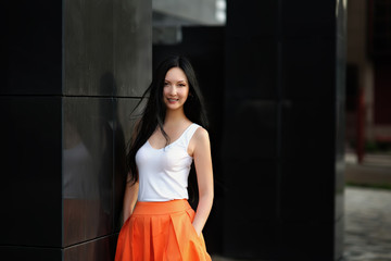 Beautiful girl in a fashionable clothing. Portrait a lady with long hair. White tank top with orange high waist skirt