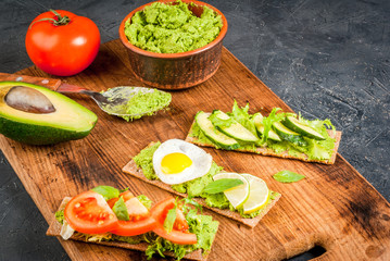Healthy Eating, Diet sandwiches on gluten-free loaves - with guacamole, fresh vegetables (tomato, cucumber), egg, lime, lettuce and basil, On a stone (concrete) gray table, copy space
