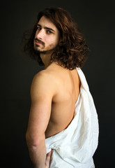 photo of handsome guy with curly hair in a white drapery half turned