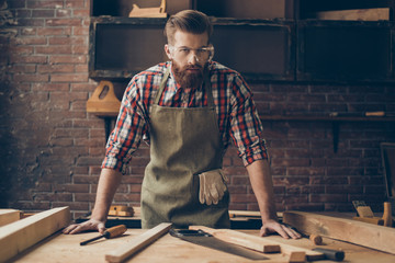 Bearded handsome cabinetmaker at the tabletop with tools.  Stylish craftsman with brutal hairstyle...
