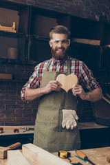 Happy handsome joiner in love holding and showing wooden heart near tabletop with tools.  Stylish...