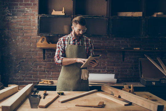 handsome cabinetmaker look at digital tablet  Stylish craftsman with brutal hairstyle and saved glasses work at his workplace