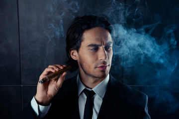 Young attractive successful businessman in suit holding cigar