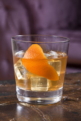 Vodka glass with orange peel is near the purple sofa.