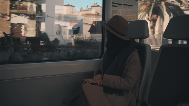 Thoughtful traveller girls smiles and sits near window in moving train car, looks outside, arrives at railroad station and goes out