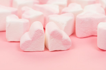 Group of heart shaped pink and white marshmallow candy on a pink background seen from the side