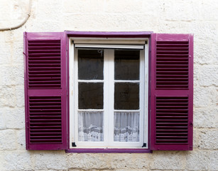 Small window with purple shutters. Facade of a building with windows.