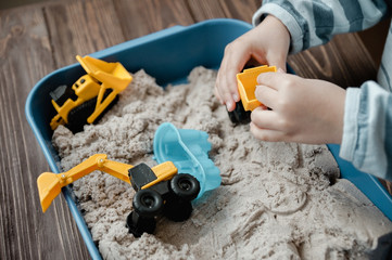 Child playing with kinetic sand and toy construction machinery