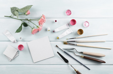 Workplace with easel, paintbrushes, roses and paints on wooden boards