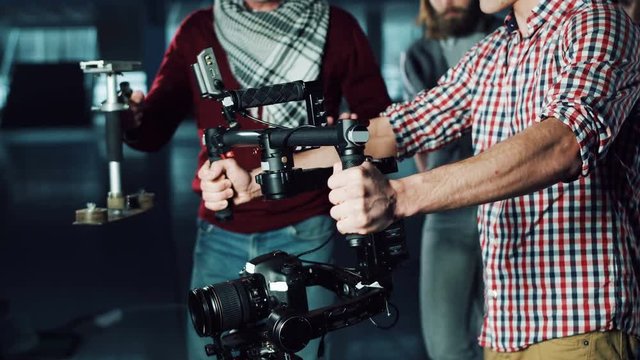 Man testing handheld camera gyro stabilizin gimbal, stretching arms with device and following the moves of stage director