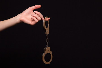 Female hand holding handcuffs on a dark background