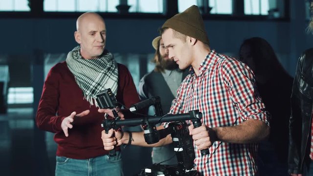 Man testing handheld camera gyro stabilizin gimbal, stretching arms with device and following the moves of stage director