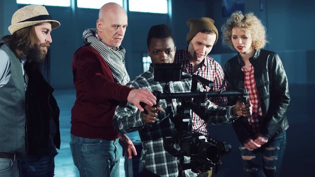 African young man testing handheld camera gyro stabilizin gimbal, the director shows a difference between the mechanical and electronic three-axial video stabilizer