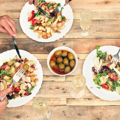 Top view of plates of salad, olives, three glasses of champagne on wooden table. Dinner concept