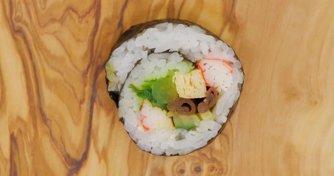 Sugoi japanese sushi roll with several ingredients rotating on a olive wood surface
