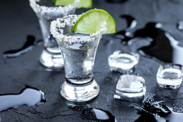 Silver tequila shots with ice and lime on black table background