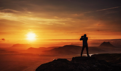 Happy man standing on a cliff at sunset. - obrazy, fototapety, plakaty