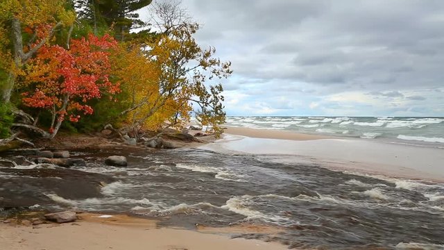 The Hurricane River flows out from woods with fall colors and across the beach and into Lake Superior at Pictured Rocks National Lakeshore in the Upper Peninsula of Michigan.