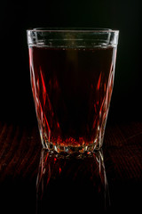 A glass with red drink on a dark background.