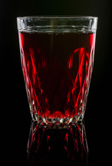 A glass with red drink on a dark background.