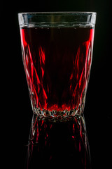 A glass with red drink on a dark background.