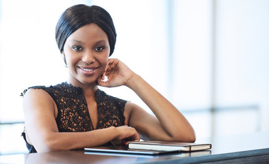 Successful black businesswoman looking into camera while seated at counter with bright backlighting...