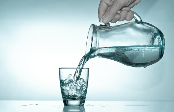Hand fills a glass with water from a glass pitcher