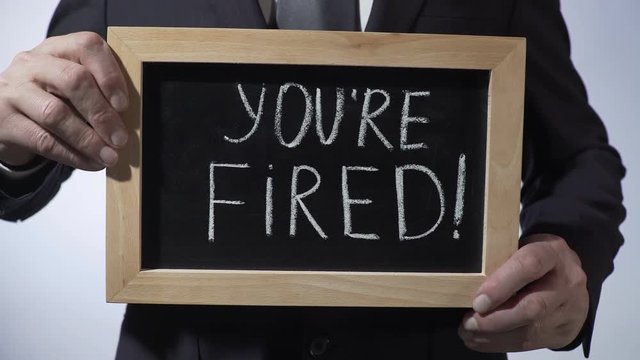 You're fired written on blackboard, businessman holding sign, business concept