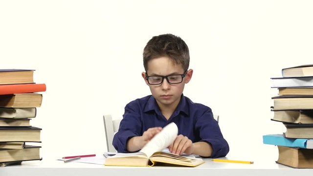 Boy sits at the table leafing through the book. White background