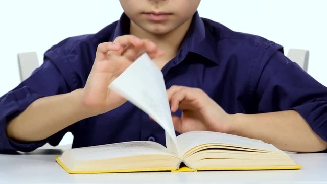 Small boy sitting at a table and reads interesting book slowly. White background. Close up