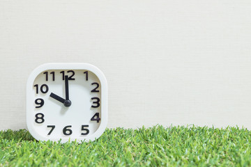 Closeup white clock for decorate in 10 o'clock on green artificial grass floor and cream wallpaper textured background with copy space