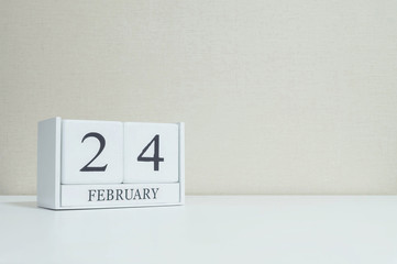 Closeup white wooden calendar with black 24 february word on blurred white wood desk and cream color wallpaper in room textured background with copy space in selective focus at the calendar