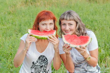 Две девушки на природе едят арбуз и смеются.