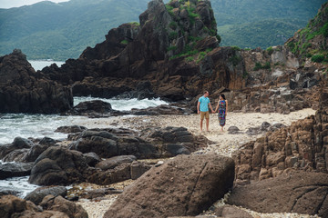 Young couple in love holding hands, walking on a sea beach in summer. The man in the blue shirt and the girl in a dress. Concept of honeymoon