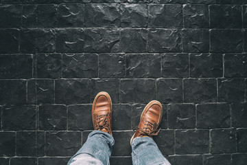 Man leg with brown boots,Black Stone floor texture,Selective focus on boots,Vintage color tone.