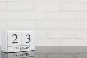 Closeup white wooden calendar with black 23 february word on black glass table and white brick wall textured background with copy space in selective focus at the calendar