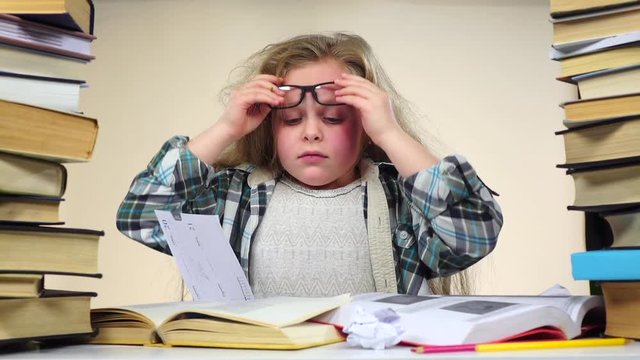 Girl sits at a table with books and nervous. Blue background. Slow motion