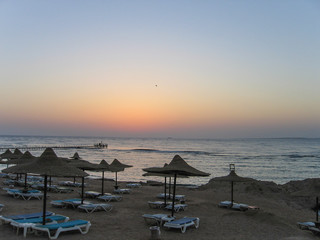 Fototapeta na wymiar Red Sea in Egypt during sunrise with blue water and beach with umbrellas and chairs