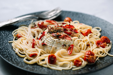 Spaghetti with roasted ricotta and tomatoes on a black plate 