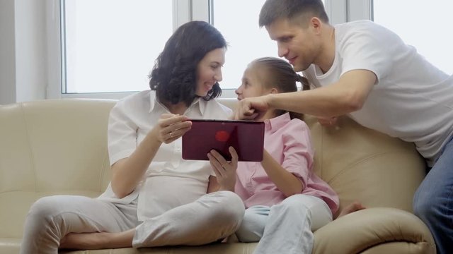 Parents showing digital tablet to their daughter at home.
