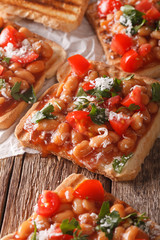 toasts with beans in a tomato sauce, cheese and herbs closeup. vertical