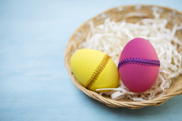 Closeup colorful Easter egg on rattan basket over blue background