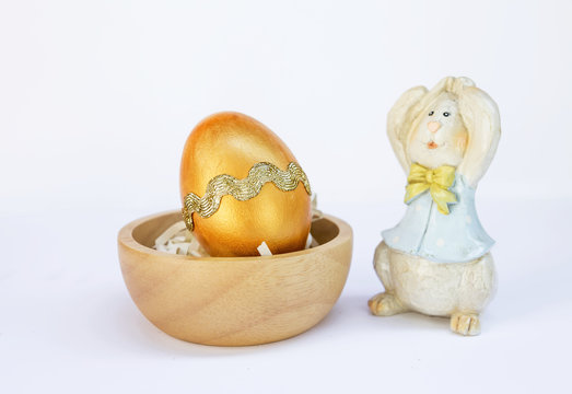 Golden Easter egg and wooden bunny on white background