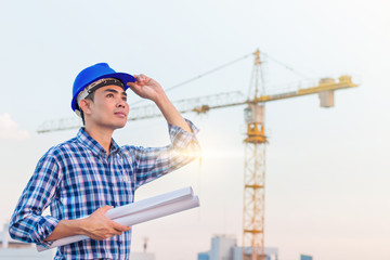 Portrait of engineer wear blue safety helmet and hold the blueprint with commitment on construction site with crane background