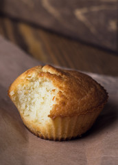 nibbled muffin on a piece of paper on a brown wooden background