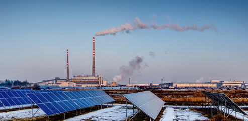 solar panels and coal power plant with smoking chimneys as a panoramic view, ecological and outdated way of getting electricity